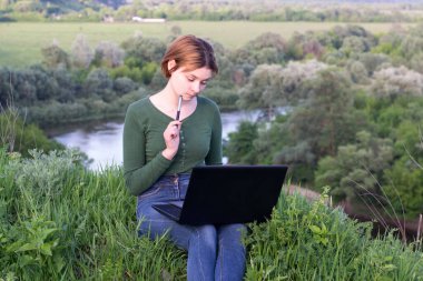Güzel kız çimlerin üzerinde otururken grafik tabletini kullanıyor.