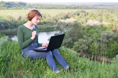 Güzel kız çimlerin üzerinde otururken grafik tabletini kullanıyor.