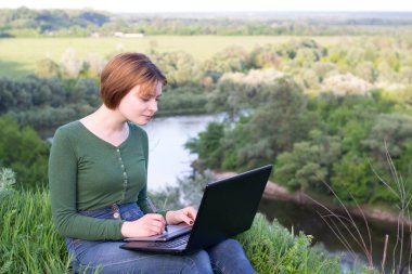 Güzel kız çimlerin üzerinde otururken grafik tabletini kullanıyor.