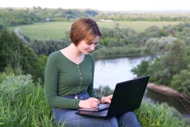 Güzel kız çimlerin üzerinde otururken grafik tabletini kullanıyor.