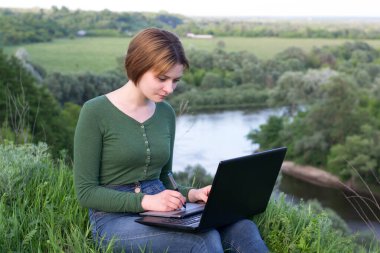 Güzel kız çimlerin üzerinde otururken grafik tabletini kullanıyor.