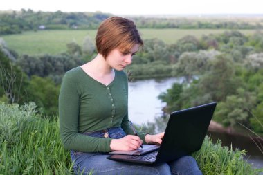 Güzel kız çimlerin üzerinde otururken grafik tabletini kullanıyor.