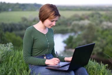 Güzel kız çimlerin üzerinde otururken grafik tabletini kullanıyor.