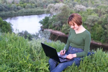 Güzel kız çimlerin üzerinde otururken grafik tabletini kullanıyor.