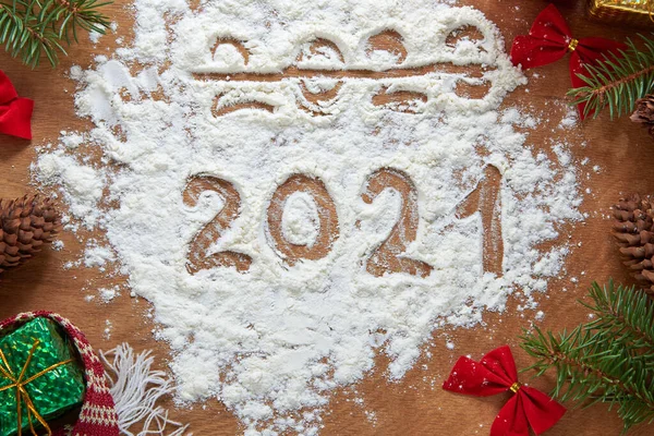 2020 crossed out, New Year 2021 written on flour. Snowman, cones, branches of a Christmas tree, bows and gifts on a wooden background. Christmas background.