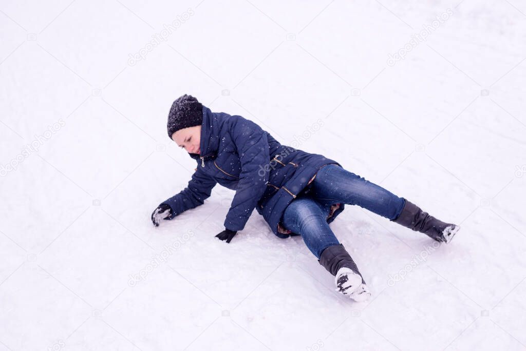 The girl slipped on ice covered with snow in the street, falling and injury in the winter