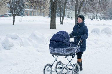 Genç bir anne, karlı bir kış gününde bebek arabasıyla yürür.
