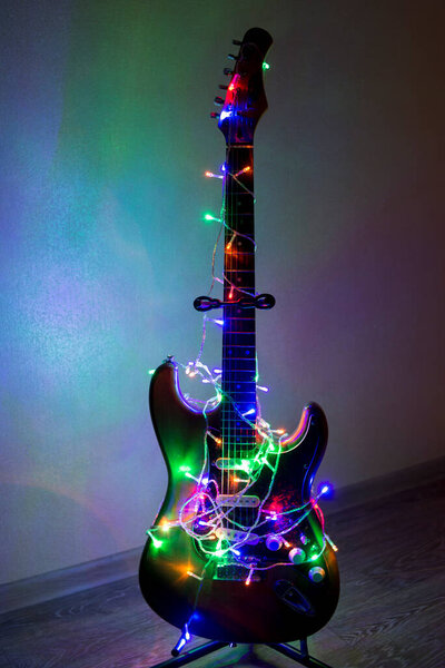 Electric guitar wrapped in colorful bright garland, the idea of holiday music