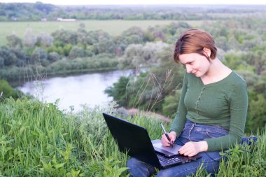 Güzel kız çimlerin üzerinde otururken grafik tabletini kullanıyor.