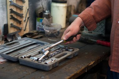 Tamirci set araçlarından araç alır, garajdaki masaüstünde yatar