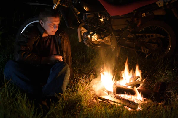 那家伙坐在火炉边和摩托车旁边喝茶 — 图库照片
