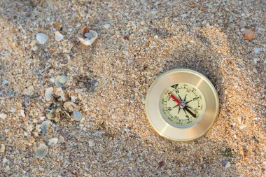 Yönü gösteren bir pusula deniz kabuklarıyla kumların üzerinde yatar.