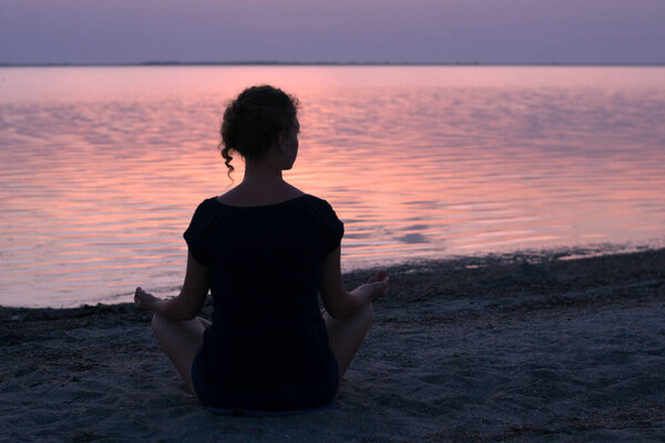 A girl sits on the lake shore and meditates