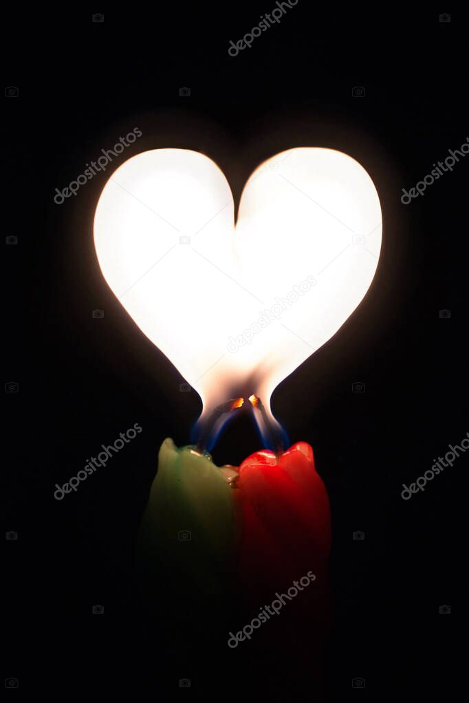 Two colored burning candles with a flame in the form of a heart on a black background