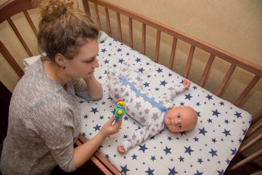 Annem beşikte yatan yeni doğmuş çocuğuna çıngırak gösteriyor.