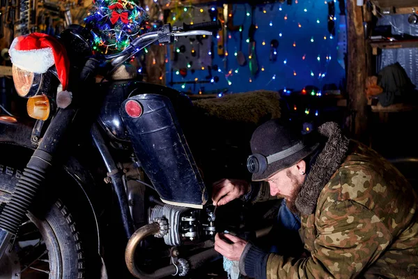 A man repairs an old motorcycle in the garage on New Year's Eve.