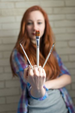 Üzerinde çizim fırçası olan parlak tişörtlü kızıl saçlı bir kızın fotoğrafı.