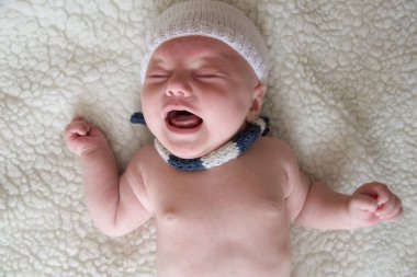 Şapkalı ve fularlı yeni doğmuş bir bebek arka planda ağlıyor.