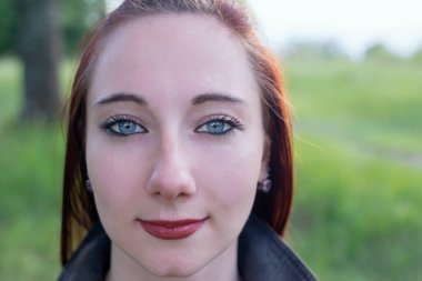 Açık havada parlak mavi gözlü kızıl saçlı bir kızın portresi.