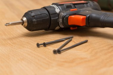 Kablosuz tornavida, ahşap bir arka planda vidaları kendi kendine vuruyor. Tamir işi ve bina teması, yakın çekim.