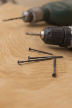 Kablosuz tornavida, ahşap bir arka planda vidaları kendi kendine vuruyor. Tamir işi ve bina teması, yakın çekim.