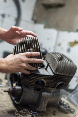 Garajda motosiklet motoru tamir eden bir adam, silindir tutan eller, yakın plan.