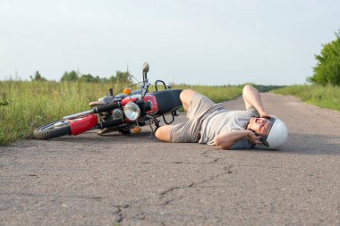 Adam asfaltta motosikletinin yanında yatıyor, trafik kazalarının teması...