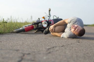 Bir adam dizine tutunur, motosikletinin yanındaki asfaltta yatar, trafik kazalarının teması