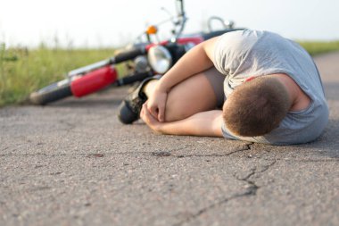Bir adam dizine tutunur, motosikletinin yanındaki asfaltta yatar, trafik kazalarının teması