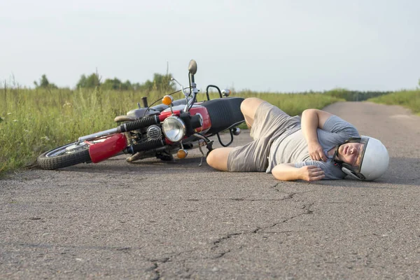那人躺在摩托车旁的柏油路上 那是一场车祸的主题 — 图库照片