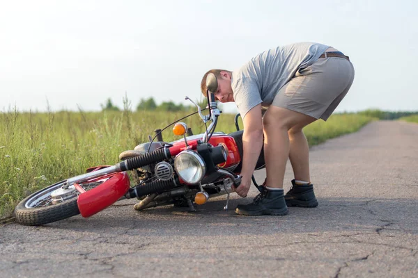一个男人举起一辆在事故后掉落的重型摩托车 — 图库照片
