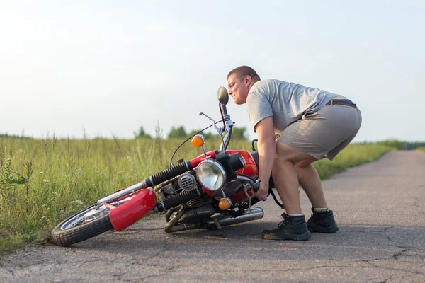 A man lifts a heavy motorcycle that fell after an accident