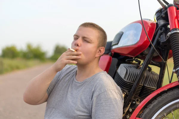 Motosikletinin Yanında Oturan Dışarıda Sigara Içen Genç Bir Adam — Stok fotoğraf