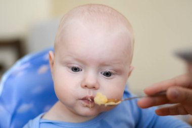Annem komik oğlunu kaşıkla elma püresiyle besler.