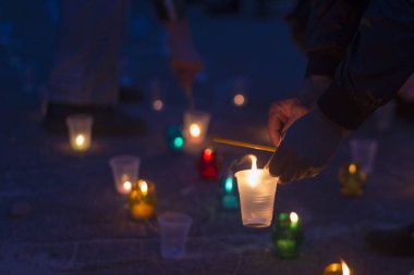Bir adam asfaltta duran bir mum yakıyor. Yakınını kaybedenler için anma günü