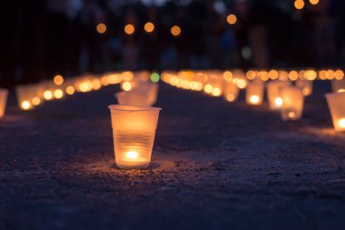 Sokakta asfaltta yanan bir grup mum ve arka plandaki insanlar. Yakınını kaybedenler için anma günü