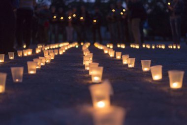 Sokakta asfaltta yanan bir grup mum ve arka plandaki insanlar. Yakınını kaybedenler için anma günü