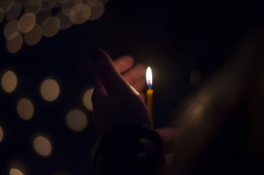 Karanlıkta yanan ince bir mumu tutan el.