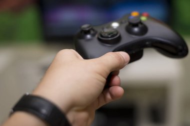 Adamın eli televizyonun önünde oynamak için siyah joystick 'i tutuyor.