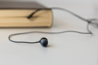 Hafif arka plan üzerine bir kitaptan çıkan siyah kulaklıklar, sesli kitap teması