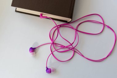 Pembe kulaklıklar bir kitaptan sarkan hafif arka plan, bir sesli kitap teması