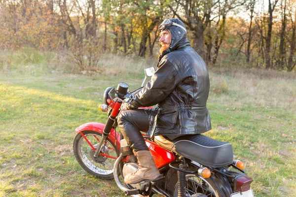 森林里骑自行车的人穿着皮夹克头戴安全帽骑着老式复古摩托车 — 图库照片