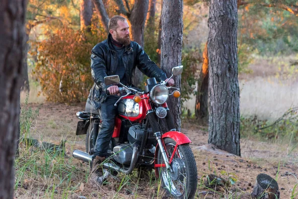 Biker in a leather jacket and helmet on a vintage retro motorcycle in the forest