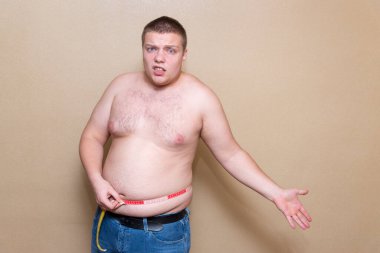 Genç bir adam göbeğini bir metreyle ölçer.