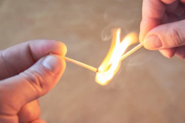 Bir erkek ve bir kadının elleri, yanan kibritleri ahşap arka planda tutuyor.