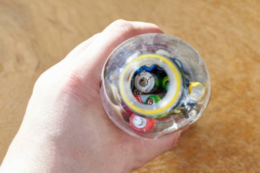 Adamın biri elinde kullanılmış pillerle dolu plastik bir şişe tutuyor, ahşap bir arka planda, çöpleri ayıklama konusu...