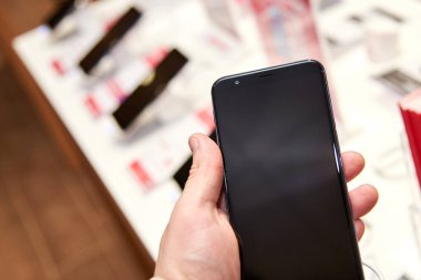 Elektronik mağazasındaki bir adamın elinde akıllı telefon, yakın plan.