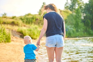 Anne ve küçük oğlu sıcak bir yaz gününde nehir kıyısında yürüyorlar.