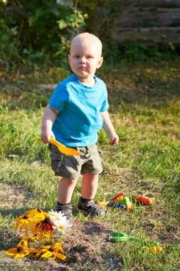 Sıcak bir yaz gününde bir çocuk çimlerin üzerinde oyuncaklarıyla oynar..