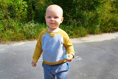 Küçük gülümseyen sevimli çocuk, bir yaz günü elde çizim yapmak için renkli tebeşirleri tutuyor. Çocuk aktivitesi.